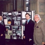 Drei Männer, Herr Mueller von der Stadt Aachen, der Redner und der Luxembuger Konsul Braun stehen im Rathaus vor einer Kollage mit Fotos aus unserer Geschichte