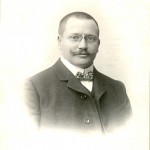 Porträt eines Mannes mit Kurzhaarschnitt, wilhelminischem Schnurrbart, Nickelbrille, Stehkragen, Fliege