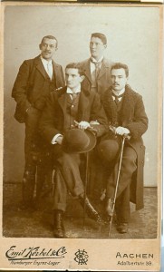 Vier Männer, zwei vorne sitzend mit Melone, zwei hinten stehend