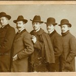 5 Männer mit Mantel und Hut hintereinander